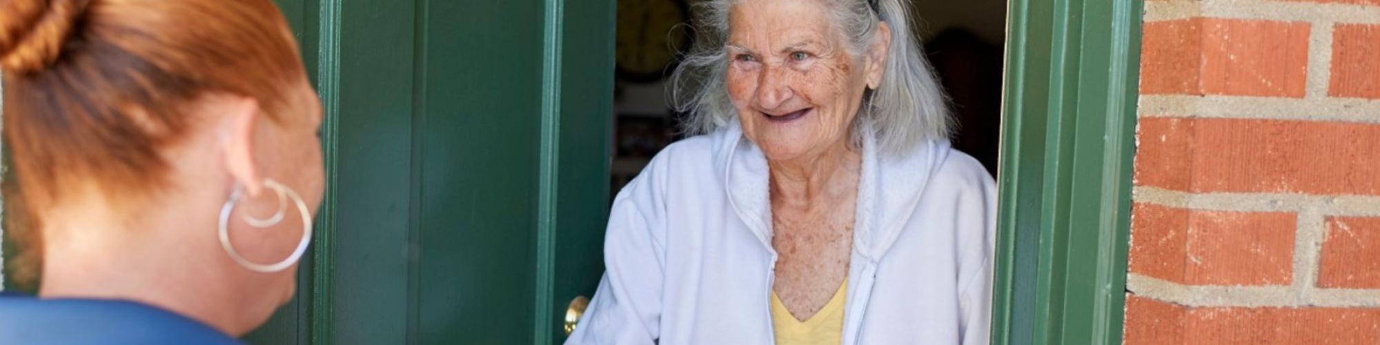 Older female client smiles at her green door as she is handed her meal from an female volunteer