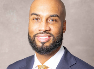 Headshot of Jason Peace smiling with a navy suit and yellow and black lined tie.