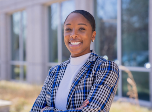 Asyia Robertson professional headshot with blue and cream plaid blazer smiling while crossing her arms.