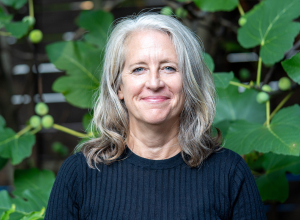 Rachel Dewees smiling in front of large deep green leaves.